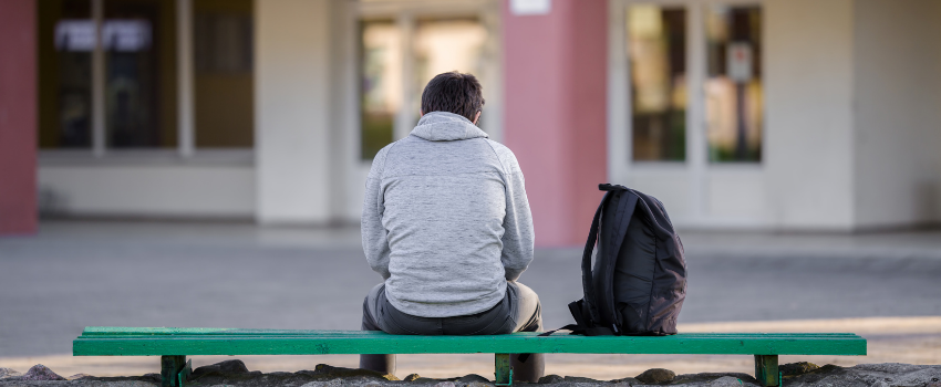 a teenage boy sitting on a bench alone outside school