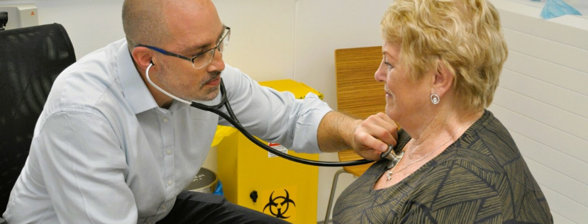 Doctor holding stethoscope to woman's chest, she is overweight