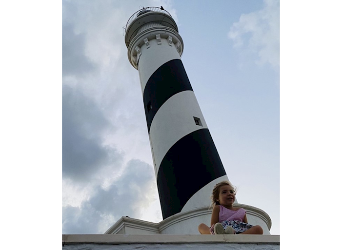 child sits in front of a lighthouse