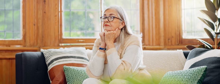 elderly woman sits of sofa looking into the distance, she looks worried