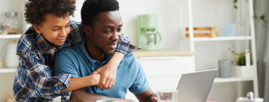 Teenager leans over shoulder of older male and they are looking at a laptop