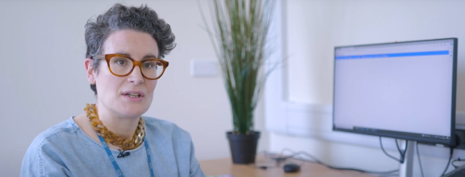 Woman talking at the camera, her computer screen is in the background